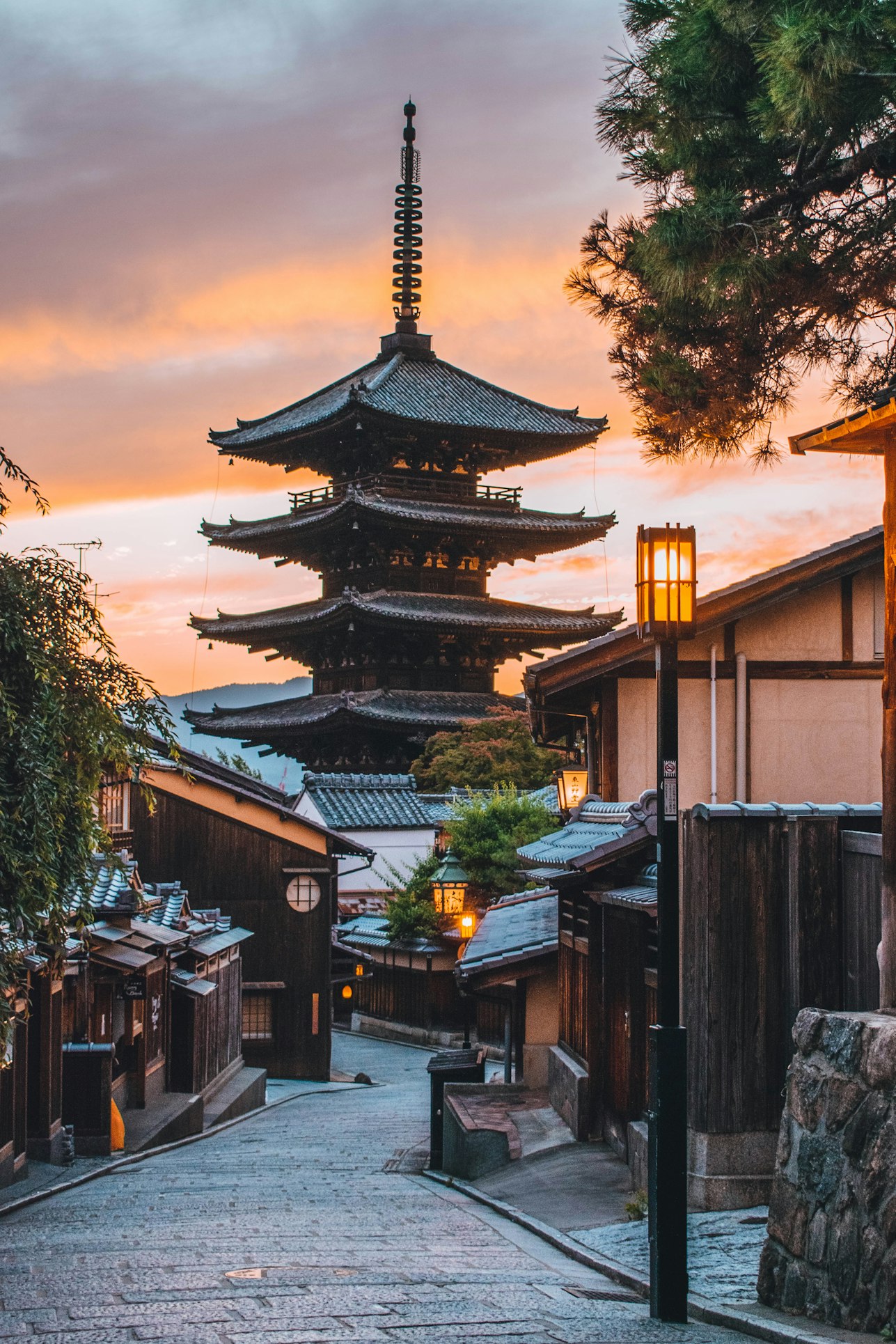 Yasaka Pagoda rising above tiled rooftops at sunset, lanterns beginning to glow.