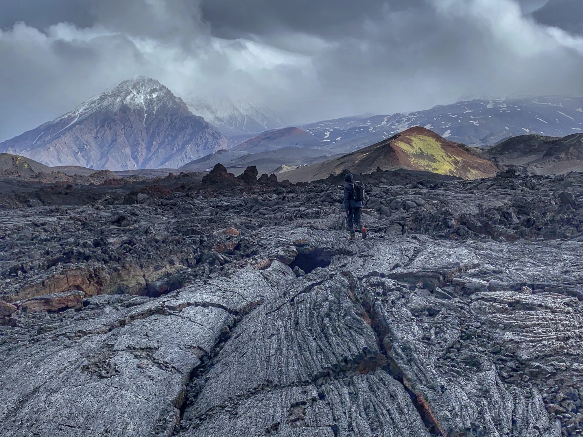 Fresh black lava field of fractured a'a rock with a smoking cone beyond.