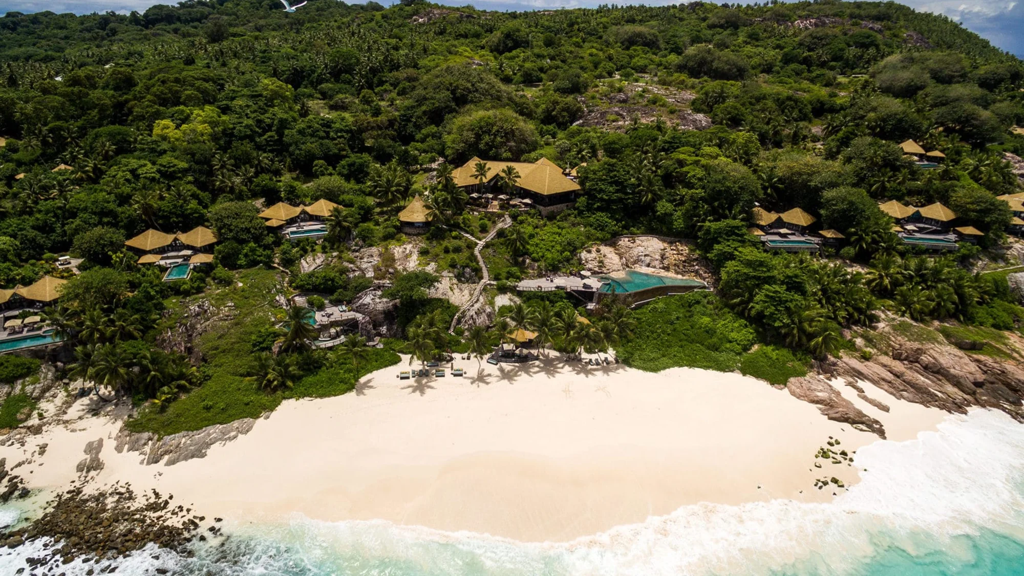 Aerial view of a tropical beach with villas and lush greenery.
