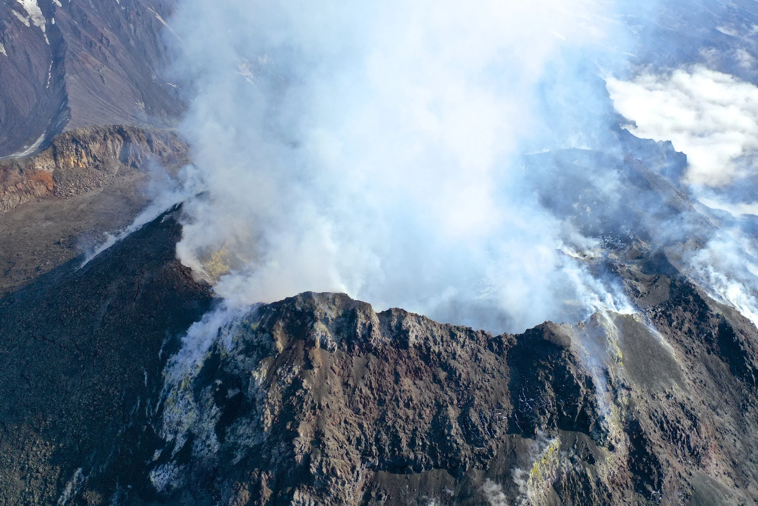 Aerial view into a steaming volcanic crater with active fumaroles.