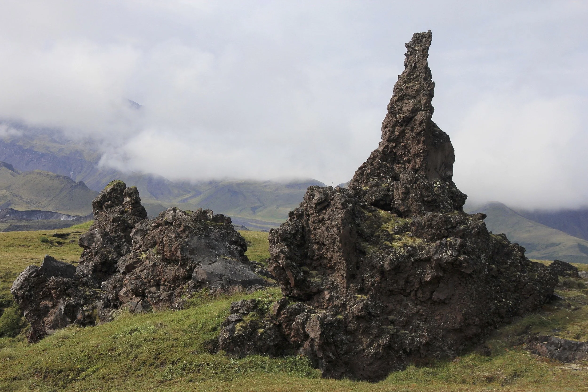 Basalt lava spire rising from a mossy volcanic plain under low clouds.