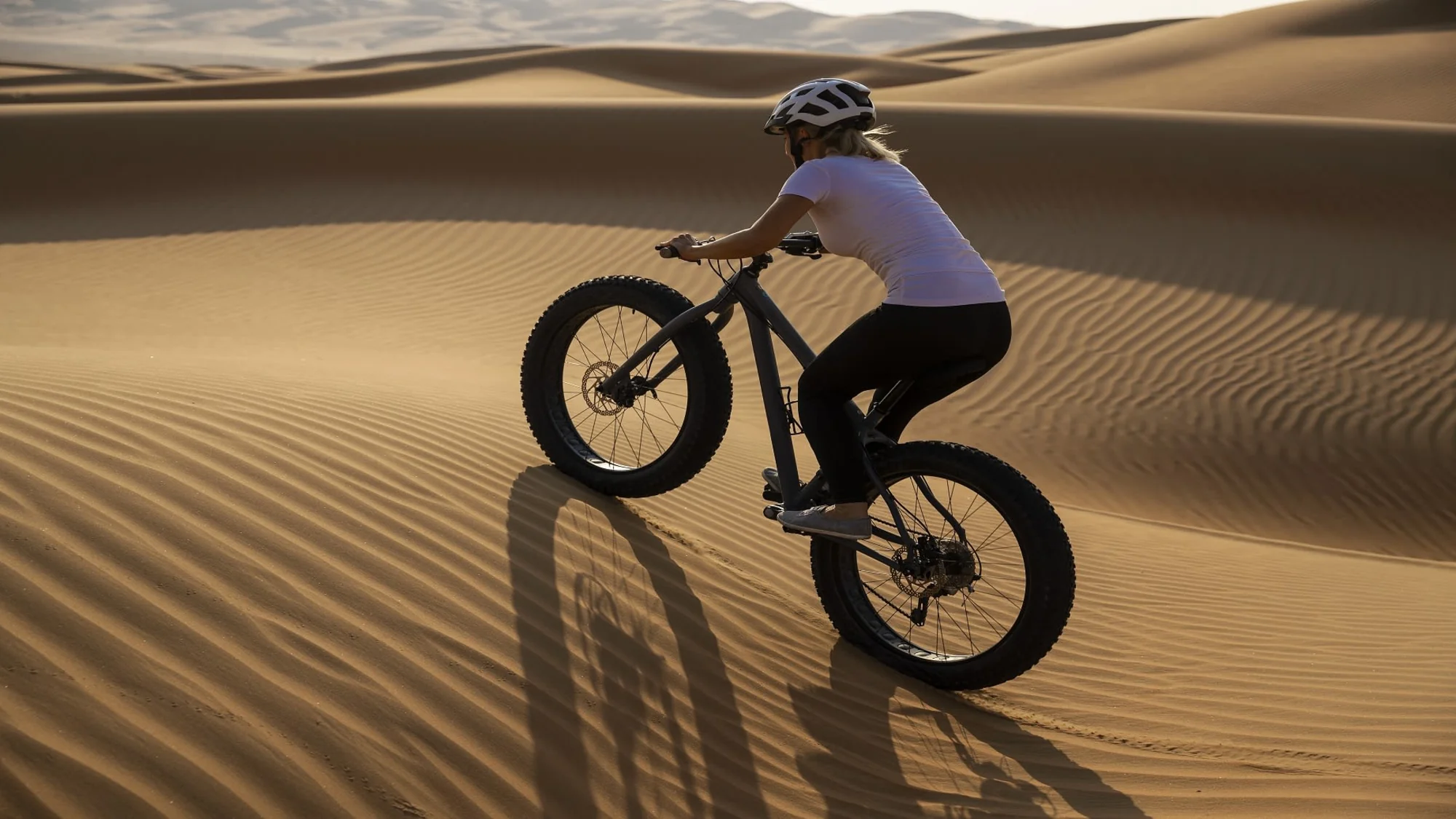 A person rides a fat bike on sand dunes during sunset.