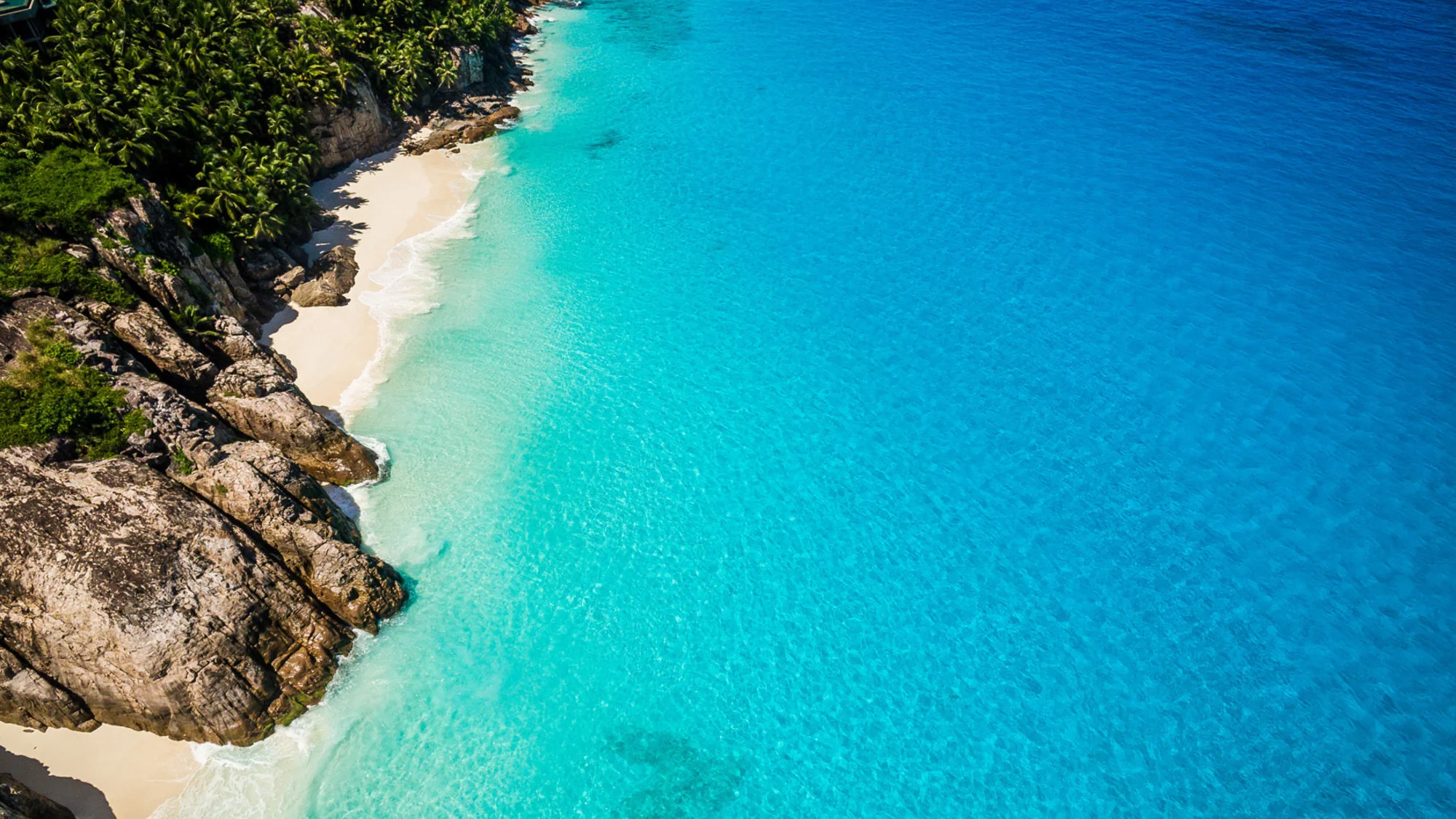 Aerial view of a tropical beach with clear blue water and rocky shoreline.