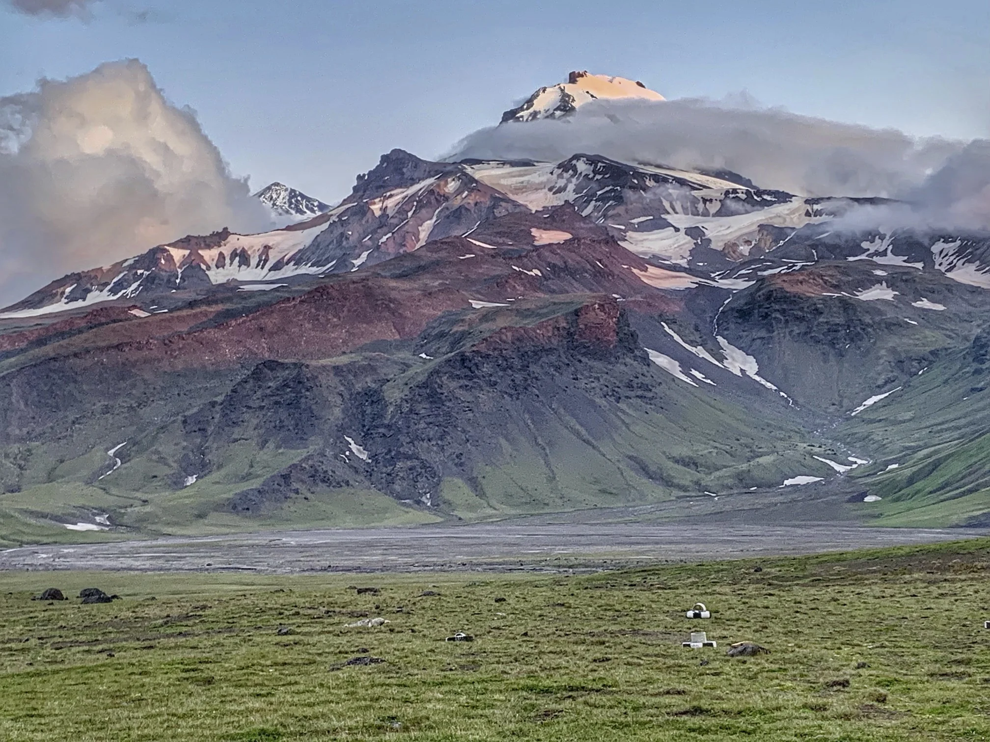 Multicolored stratovolcano with red scoria slopes, ash bands, and snow patches.