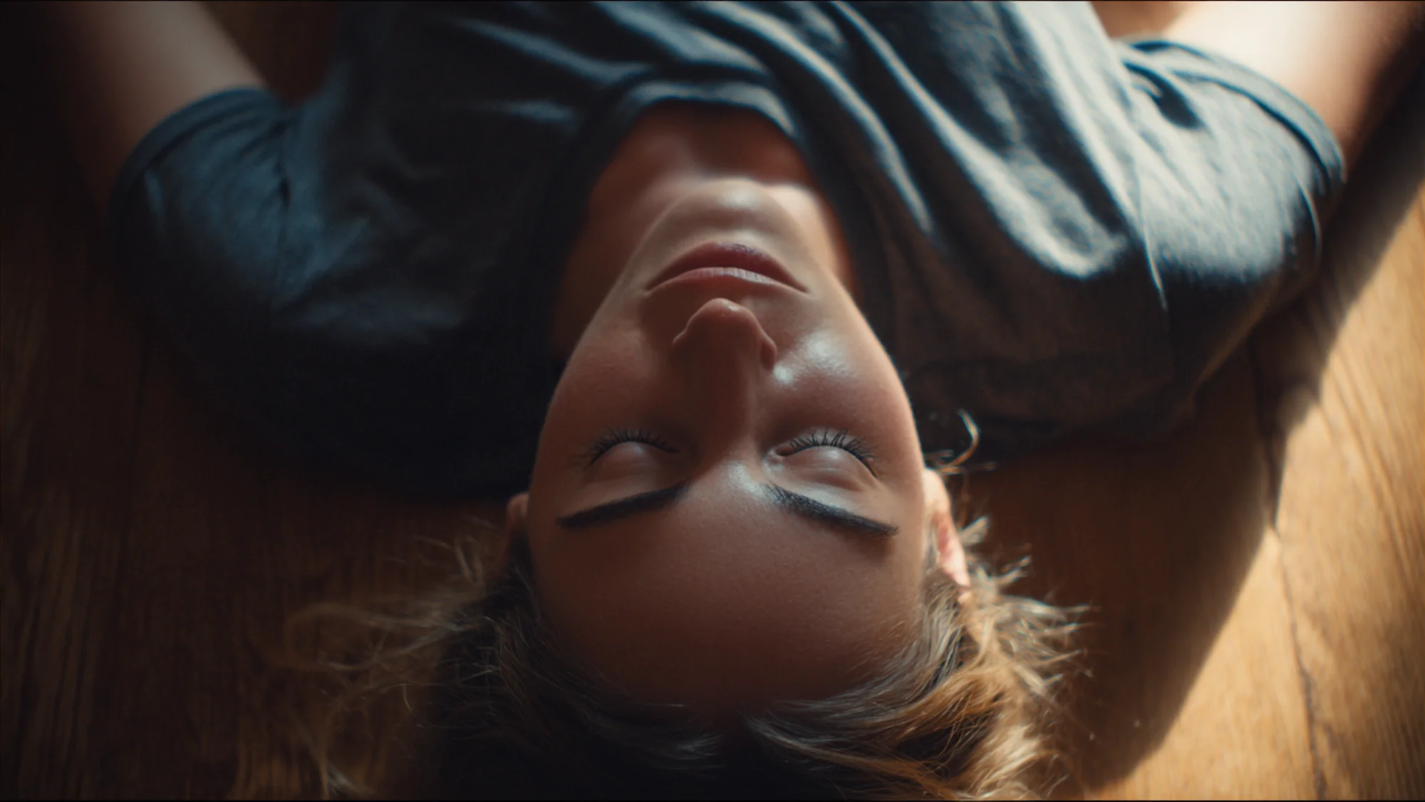 Person lying on floor from above, hands placed on lower back ribs, soft diffused natural light.