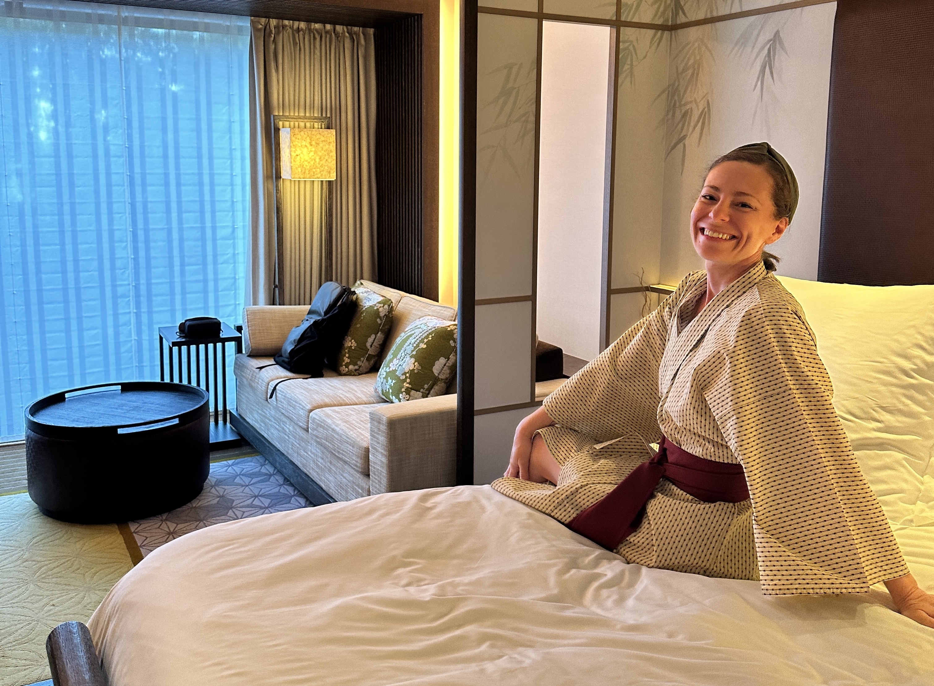 Krystal Ariel sitting on the bed at Four Seasons Kyoto in a yukata, laughing, with the Premier Heritage Garden Room and garden view behind her.