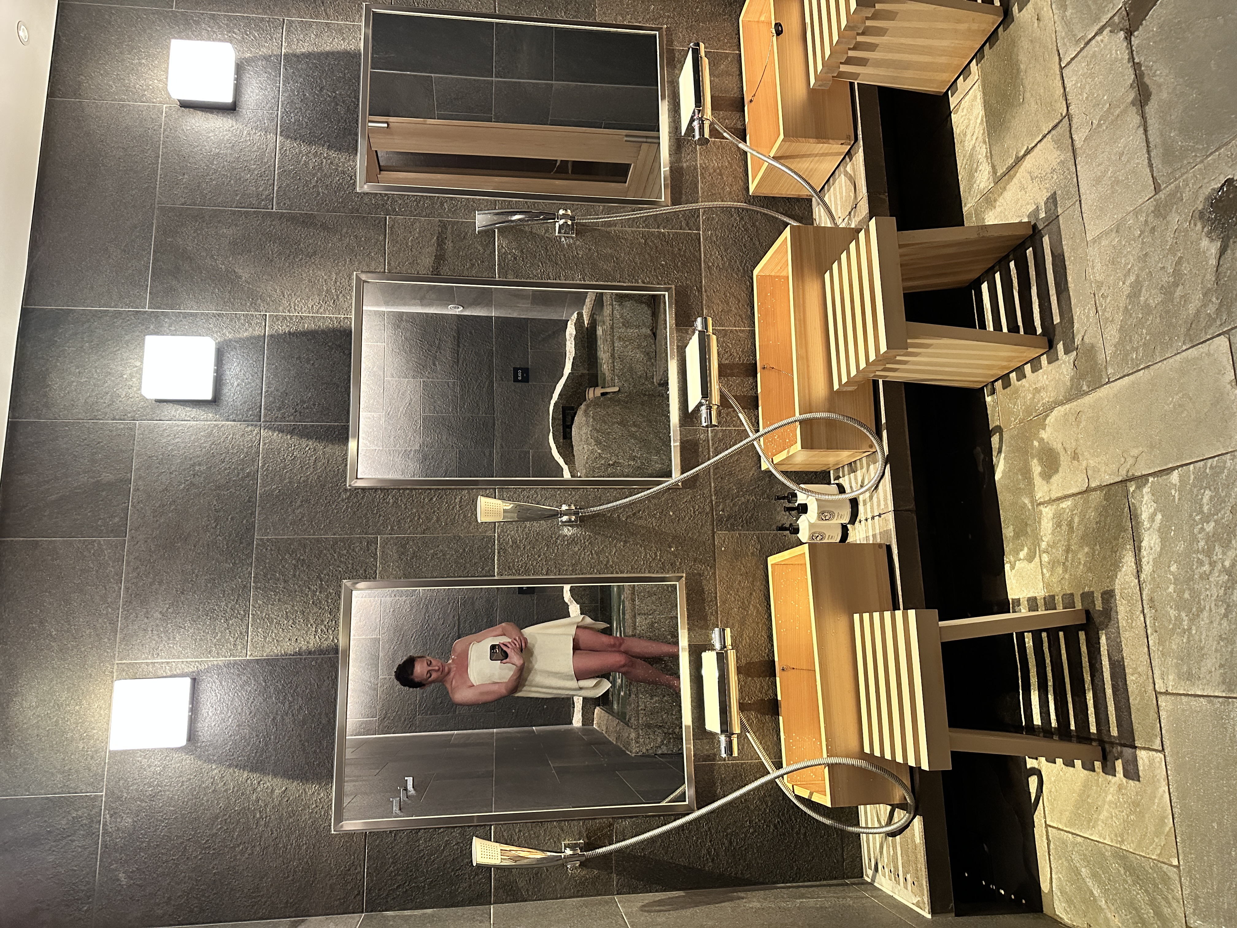 Krystal Ariel reflected in the mirror of the ofuro shower area at Four Seasons Kyoto, with wooden washing stations and dark stone walls.