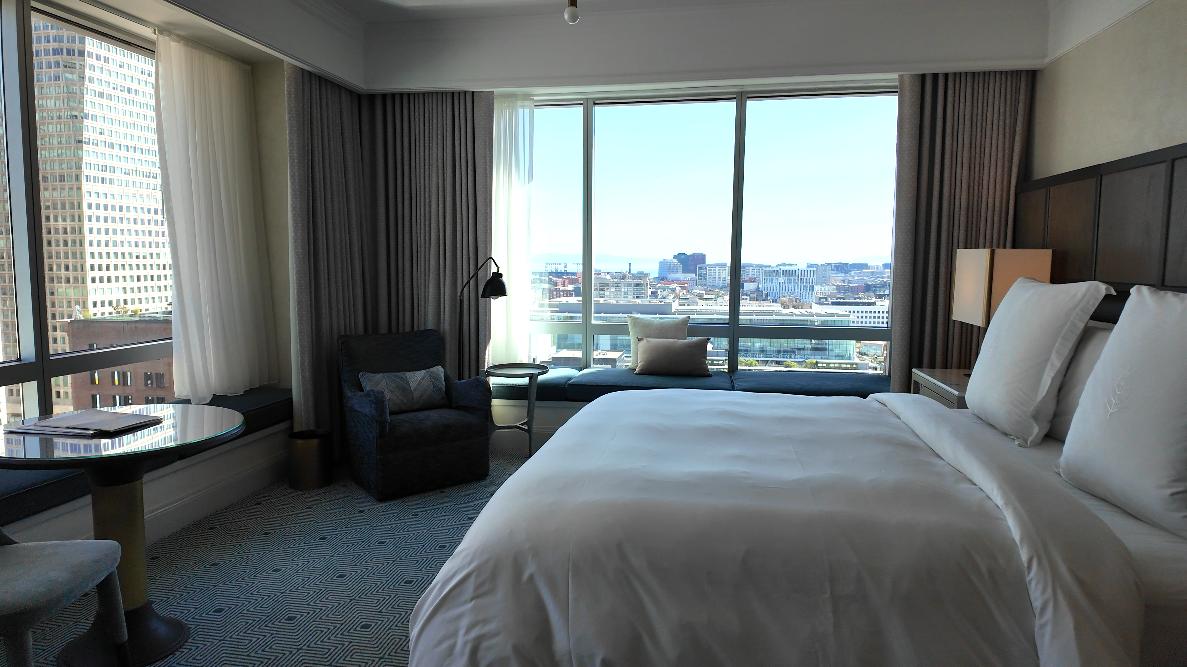 Premier Suite bedroom at Four Seasons San Francisco with a white bed, floor-to-ceiling windows, city views, and modern seating area.
