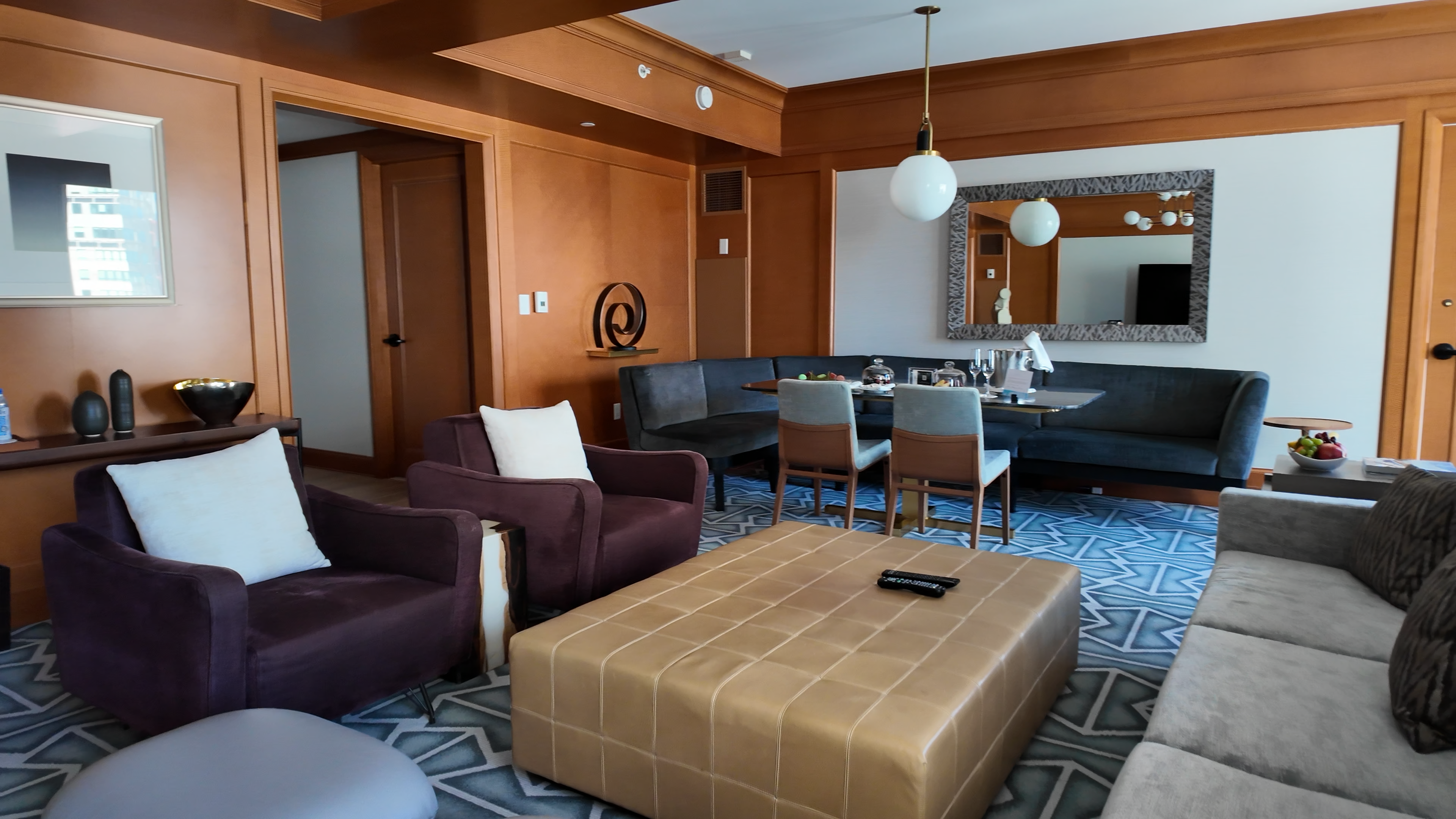 Premier Suite living room at Four Seasons San Francisco with wood paneling, dining nook, gray sofa, purple armchairs, tan ottoman, and geometric carpet.