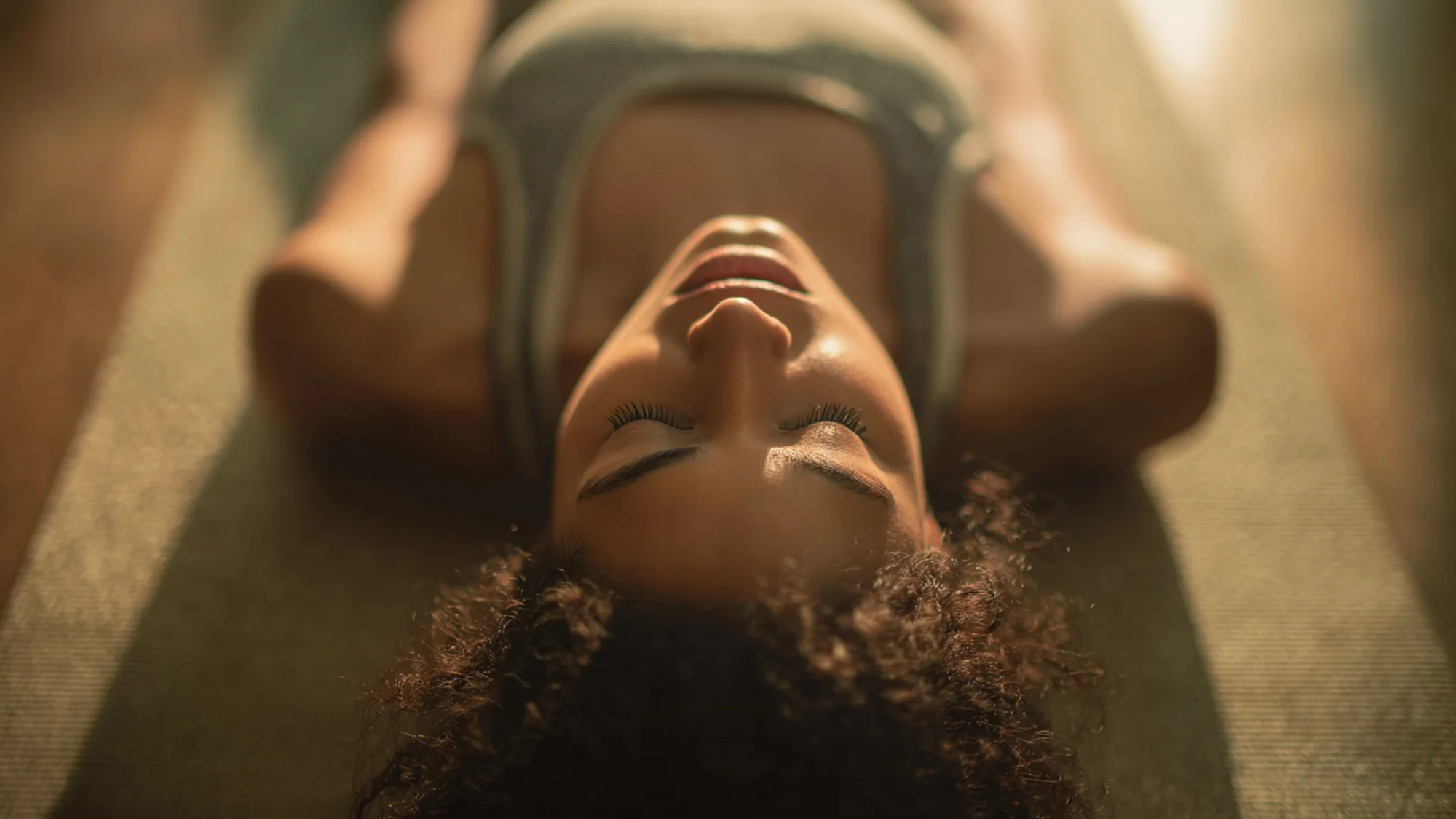 Aerial view of person in supine position on yoga mat with gentle overhead lighting.