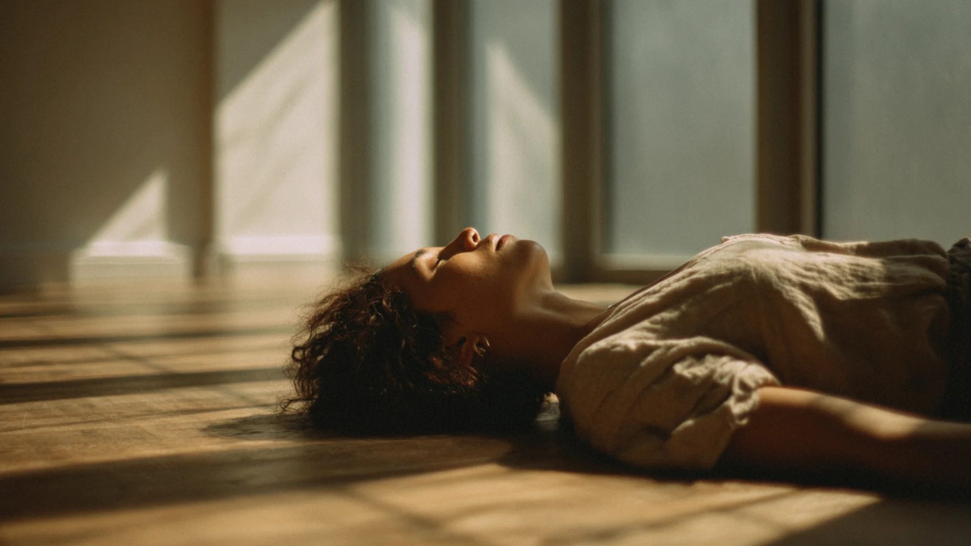 Person lying on floor in relaxed position with natural light creating soft shadows on body.